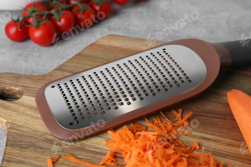 Preview: Hand grater and fresh ripe carrot on wooden board, closeup