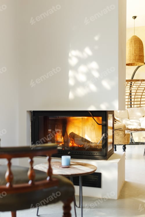 Preview: Cup of hot drink on table, warm fireplace with armchair in front and natural light from window