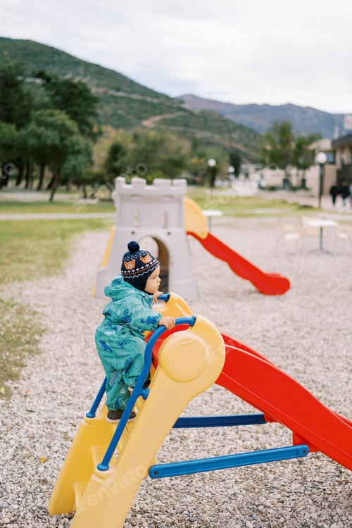 Preview: Little girl climbs the stairs to the colorful slide in the playground. Side view