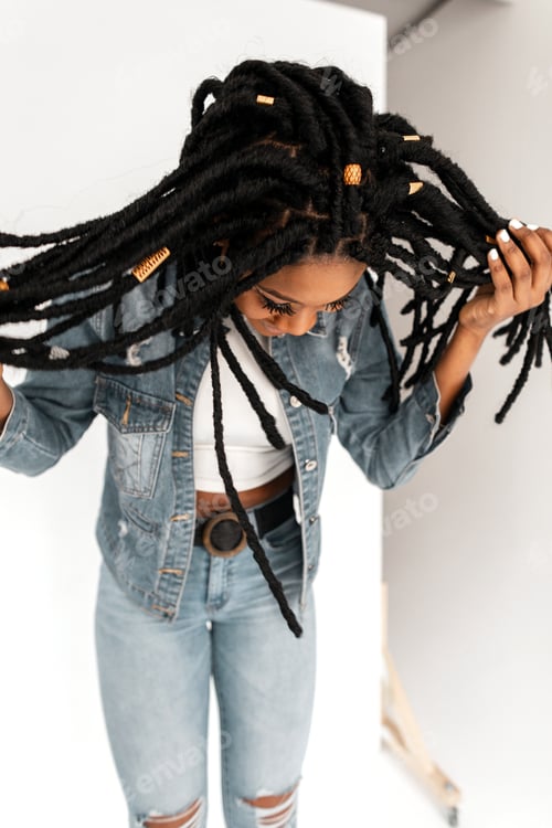 Preview: Pretty African American woman with dreadlocks in white top in blue stylish denim jeans. Girl