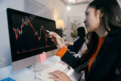 Preview: Businesswoman is pointing at a computer screen with a downward trending candlestick chart, represent