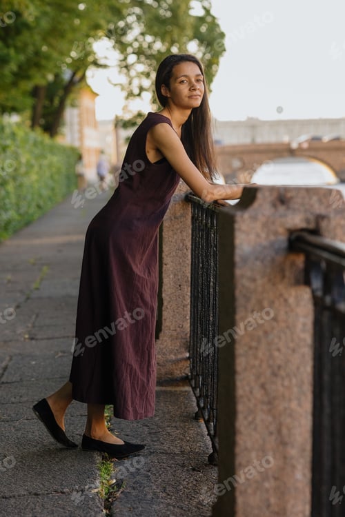 Preview: young African American woman in brown dress poses in park. happy female model at sunset in summer