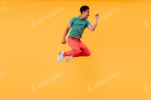 Preview: Positive african man in green t-shirt jumping in studio. Indoor shot of blissful black guy expressi