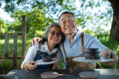 Preview: Asian retired couple is engaged in pottery making and clay painting activities.