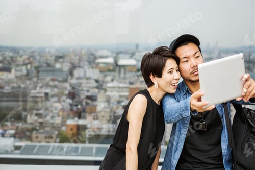 Preview: Two people taking a selfie with a digital tablet, in front of a view over a large city.