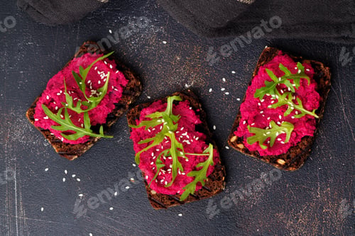 Preview: Bruschetta with beetroot hummus, arugula and sesame seeds on dark concrete background. Top view