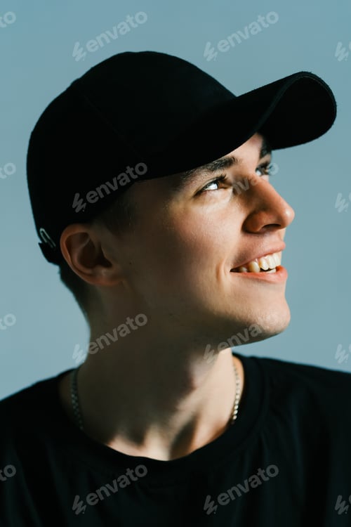 Preview: Portrait of stylish handsome caucasian man fashion model in t shirt and cap, studio shot.