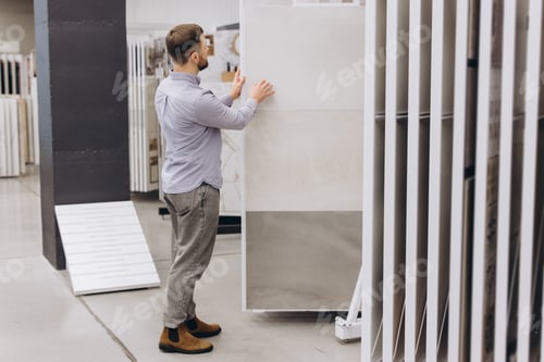 Preview: Man selecting large ceramic tiles for home renovation project, choosing flooring samples
