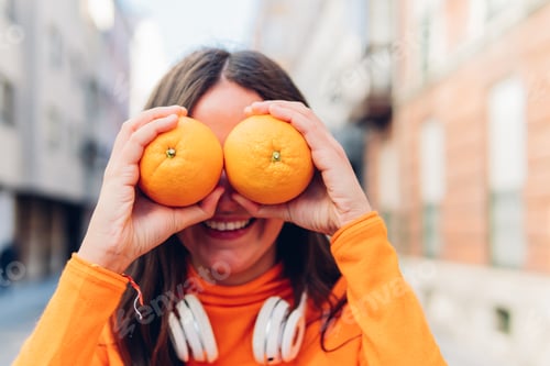 Preview: Portrait of a cheerful young woman holding two oranges to her face outdoors