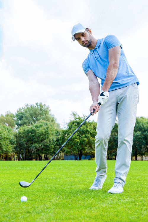 Preview: Putting green. Full length of young man in sports clothing playing golf while standing on green