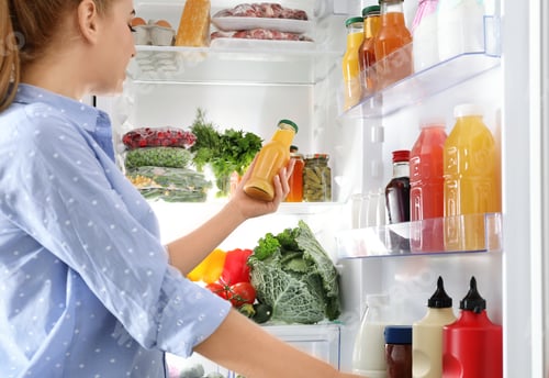 Preview: Woman taking bottle with juice out of refrigerator in kitchen
