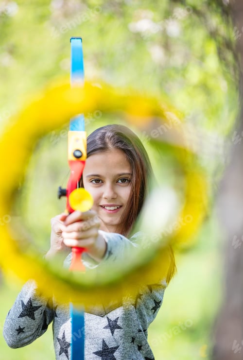 Preview: Young girl archer with bow aiming through flower wreath