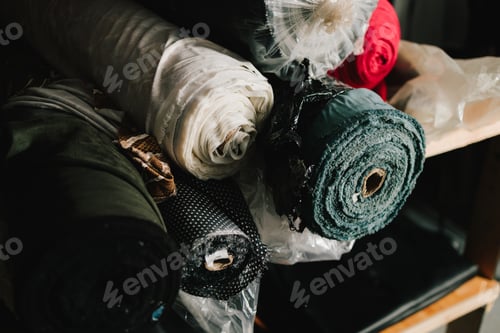 Preview: Fabric bolts arranged on workshop shelf, prepared for apparel manufacturing.
