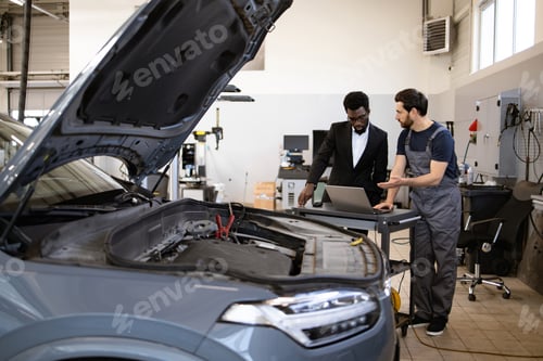 Preview: Mechanic and businessman discussing car repair in auto shop