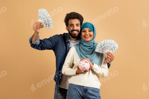 Preview: Economy Concept. Happy Young Muslim Couple Holding Cash And Piggy Bank