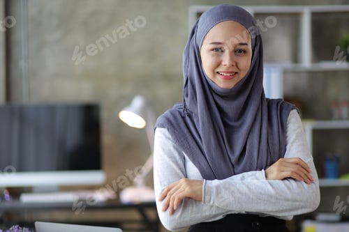 Preview: Portrait of a charming, smiling Muslim woman looking at the camera at her desk in the office.