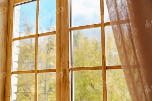 Preview: Open wooden window frame overlooking a forest with trees and blue sky and a sheer curtain blowing in