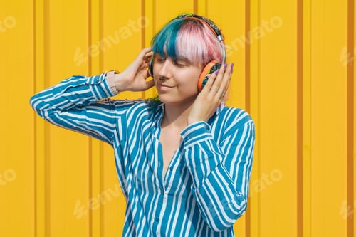 Preview: Beautiful young female with headphones enjoying listening to music standing against a yellow wall