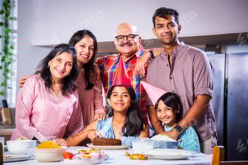 Preview: Indian asian grandparents with Family celebrating birthday by blowing candles on cake at home