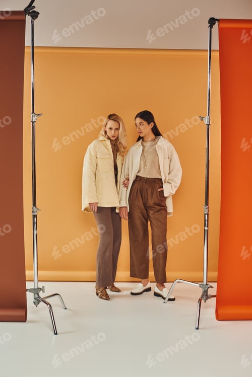 Preview: fall fashion, young and stylish women in autumn attire posing on pastel multicolored backdrop