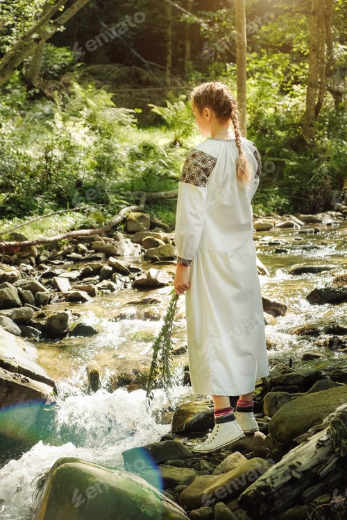 Preview: Woman in white embroidery walking by the river in the wild forest. Close to nature concept