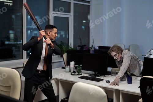 Preview: Young angry businessman with baseball bat going to hit male zombie trying to get upon desk