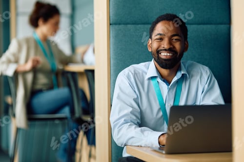 Preview: Happy black manager working on laptop in the office and looking at camera.