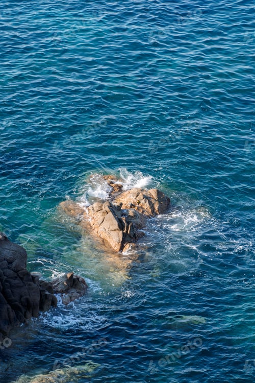 Preview: Wild rocky beach coastline and the sea, wave splashes on rock in sea shore, calm sea. Breaking waves