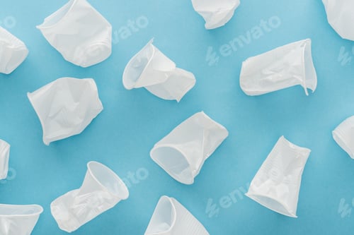 Preview: top view of white, crumpled and plastic cups on blue background