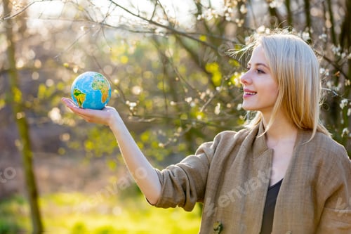 Preview: Blonde woman holds Earth globe in blooming cherry garden