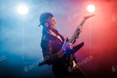 Preview: happy male rock star in leather jacket performing on electric guitar on stage with smoke and