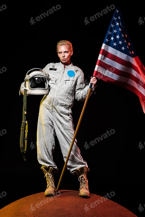 Preview: beautiful astronaut in spacesuit holding helmet and american flag on red planet