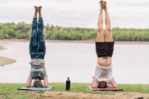 Preview: Two people with the head on the floor practising yoga in a park with a lake