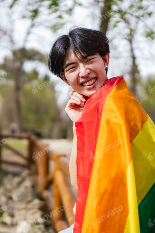 Preview: Smiling Chinese Gay Man Wrapped in Rainbow Flag, Enjoying Outdoors