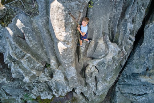 Preview: Determined boy climber clambering up steep wall of rocky mountain.