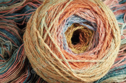 Preview: Ball of yarn from pure organic sheep's wool on an unwound skein of woolen threads. Rainbow color.
