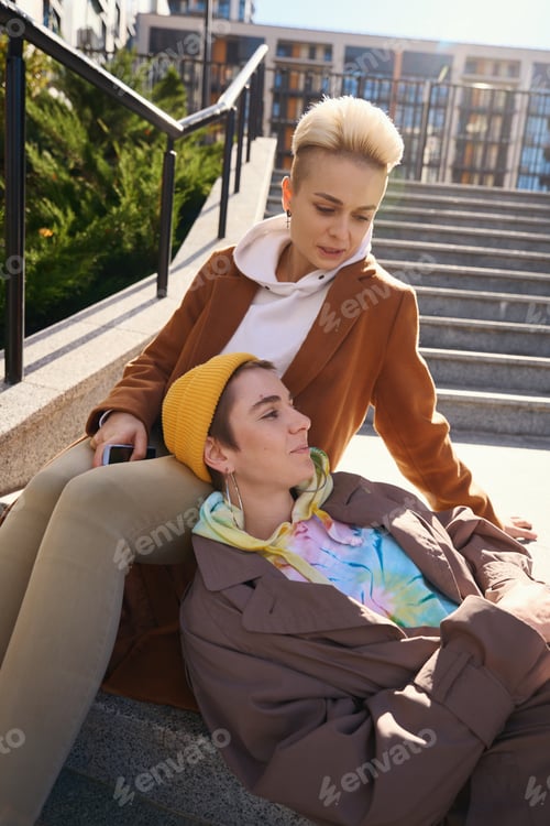 Preview: Blonde and brunette, chatting and relaxing on steps of city stairs