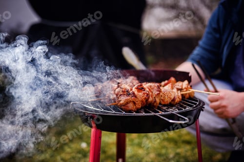 Vista previa: Persona asando jugosas brochetas de carne en una parrilla de carbón ahumado