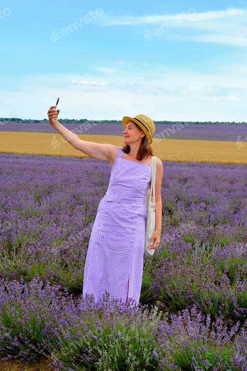 Preview: A woman takes a selfie while walking through a lavender field on a summer day