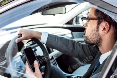 Preview: side view of businessman with smartphone driving car