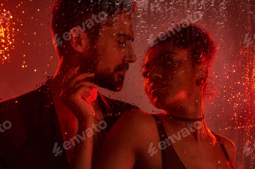 Preview: A passionate embrace between a couple behind raindrop covered glass in warm ambient lighting