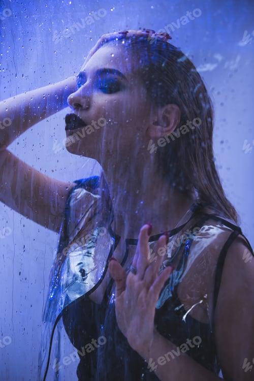 Preview: Fashionable model with wet hair dressed in black swimming suit and transparent rain coat is posing