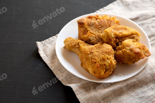Preview: Delicious homemade oven baked fried chicken on a white plate over black surface.