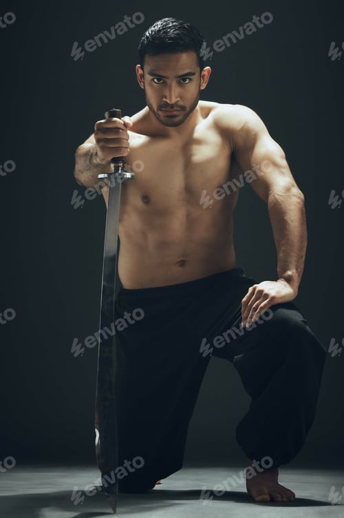 Preview: Full length shot of a handsome young man kneeling in the studio and posing with a broadsword
