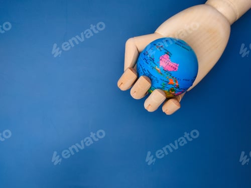 Preview: Wooden hand grasping a blue spherical globe against a vibrant blue background