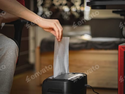 Preview: Caucasian young man inserts a sheet of paper for destruction in a black shredder