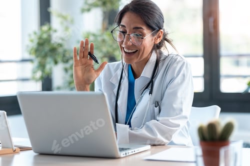 Preview: Female doctor waving and talking with colleagues through a video call with a laptop