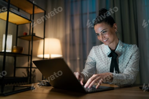 Preview: Happy mid adult business woman working on laptop in office at night
