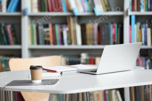 Preview: Laptop, drink and stationery on table in library