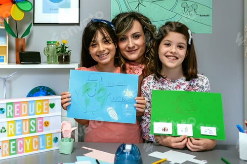 Preview: Teacher in classroom looking at camera next to students showing colorful ecological drawings